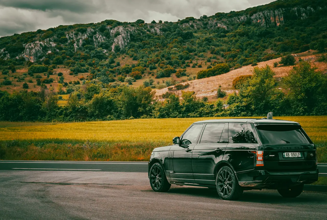 A black Range Rover parked beside fields below the hills